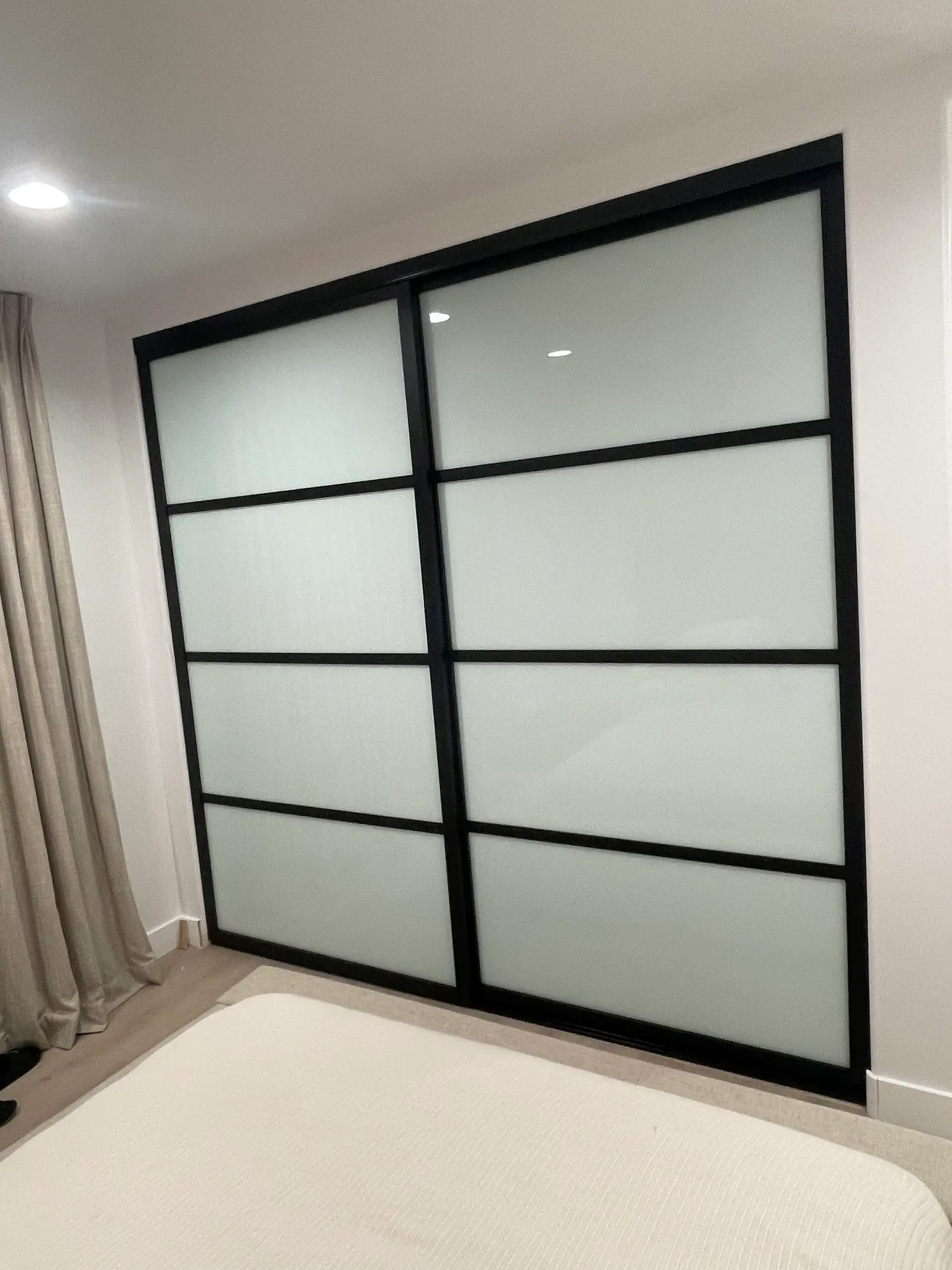 Floor-to-ceiling sliding closet doors with a black grid frame and frosted glass