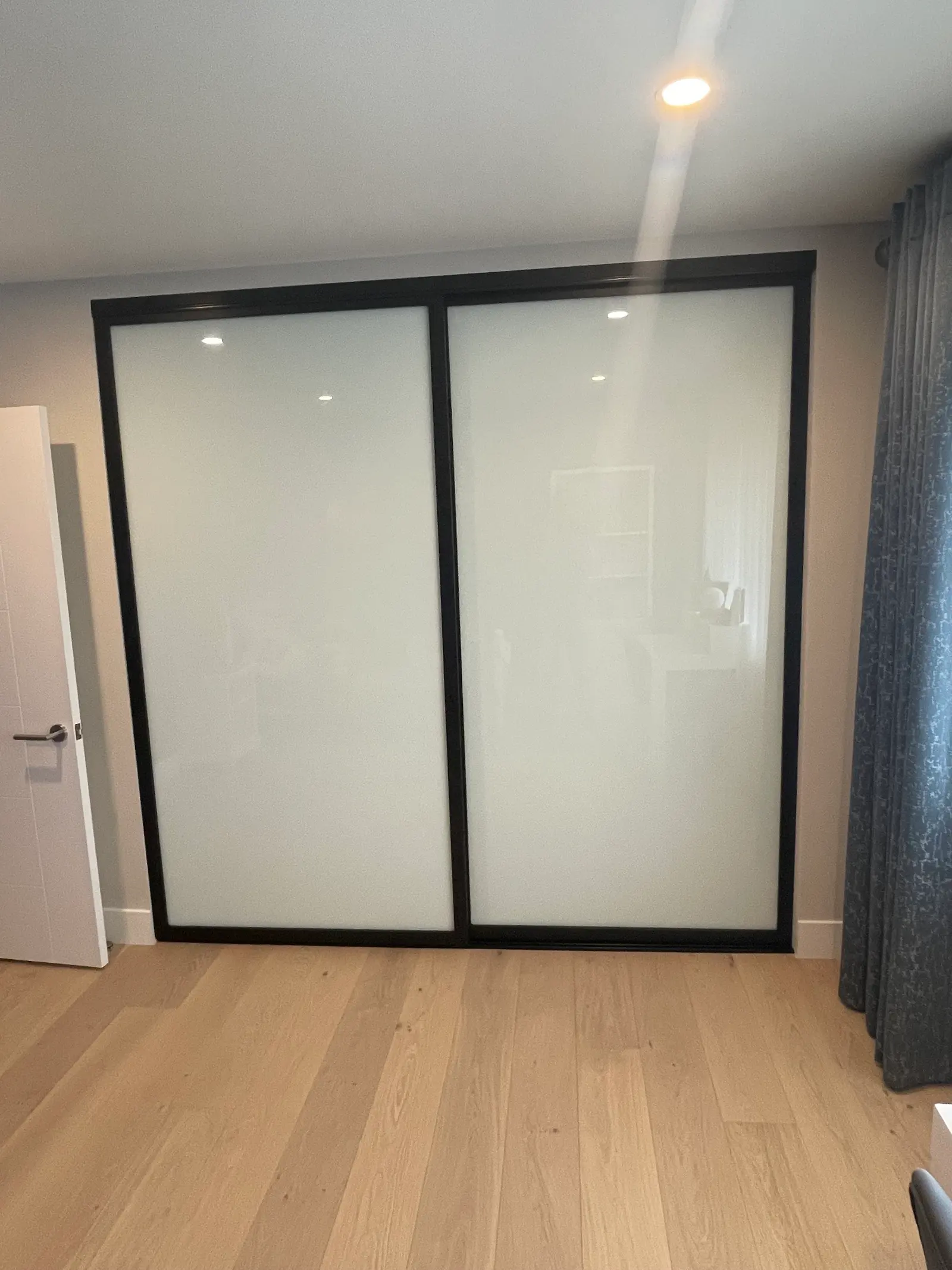 Sliding closet doors in a black frame with frosted glass panels