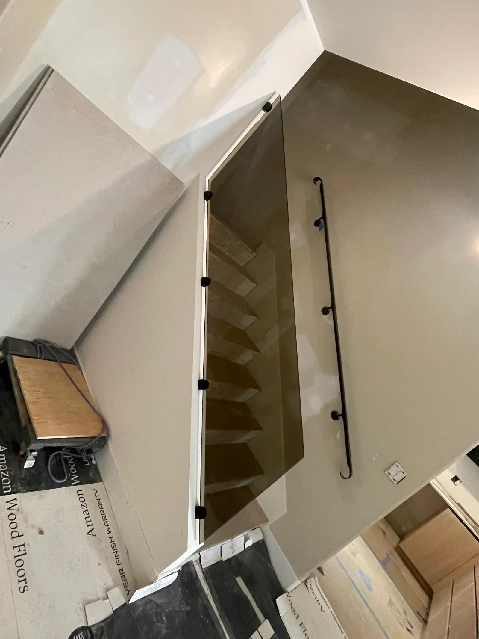 Bronze-tinted glass railing panel enclosing a stairwell, with a black wall-mounted handrail alongside