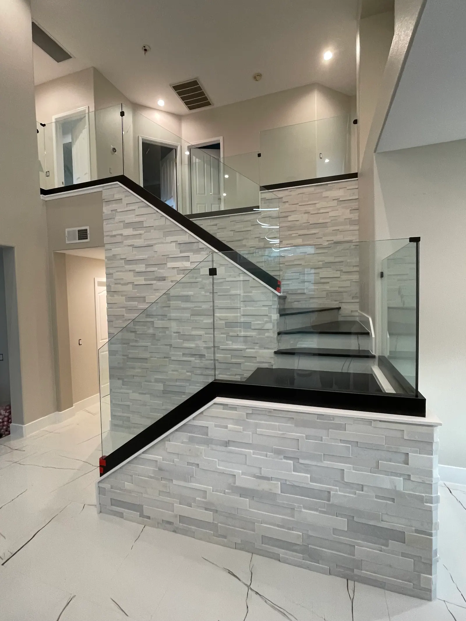 Glass stair and landing railing with a black cap rail above a stacked-stone wall