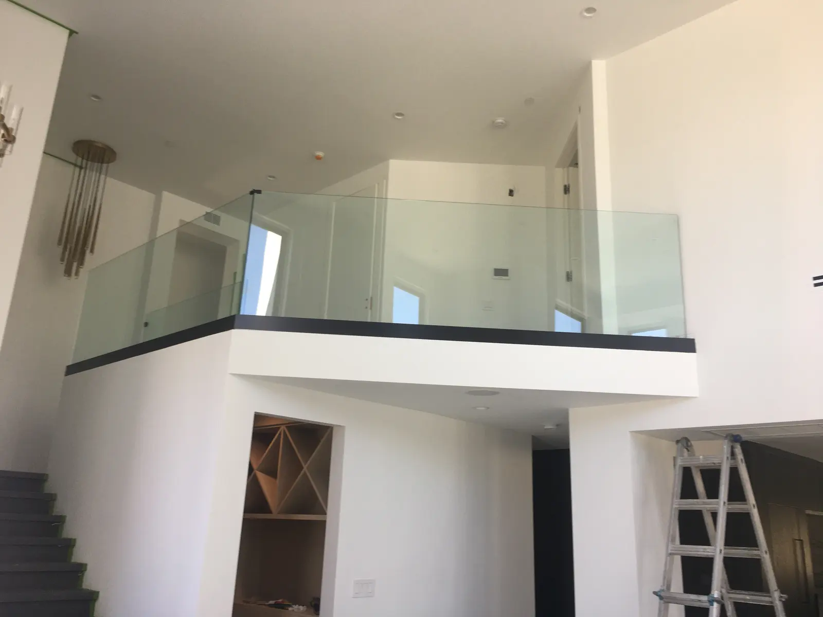 Glass mezzanine railing with a black cap rail overlooking a double-height living room