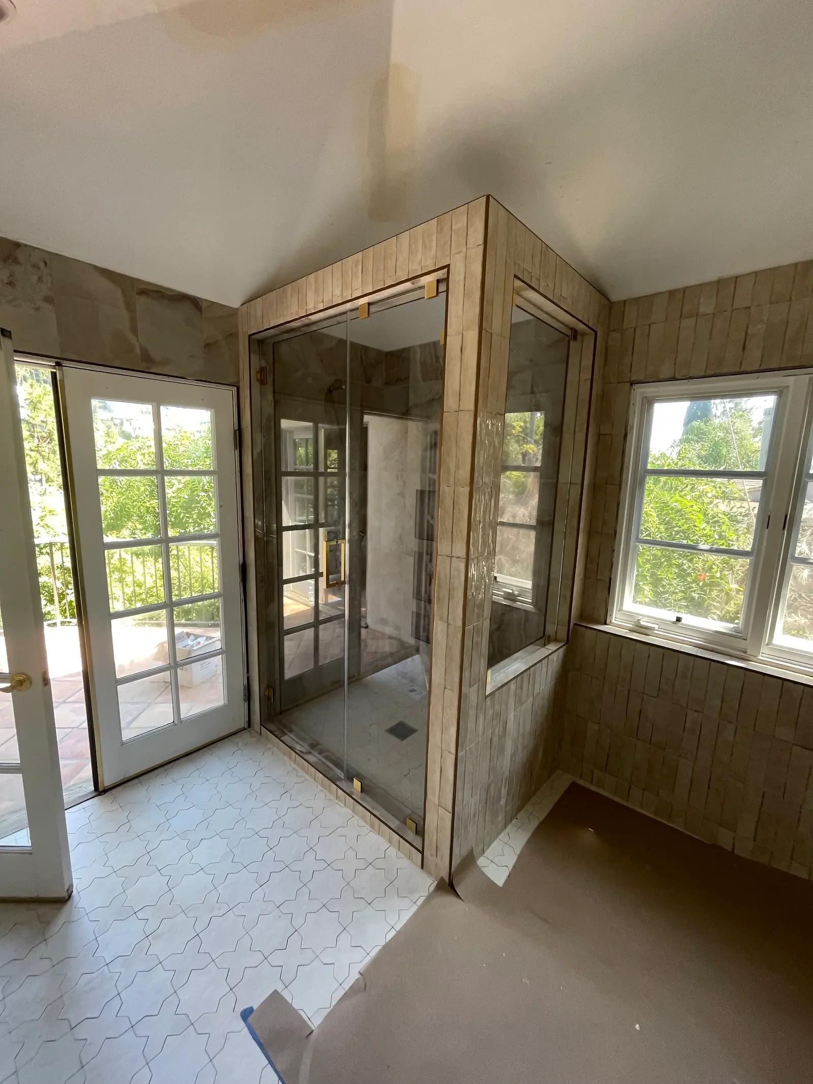 Brass-framed shower enclosure with a divided-light grid pattern beside a garden window