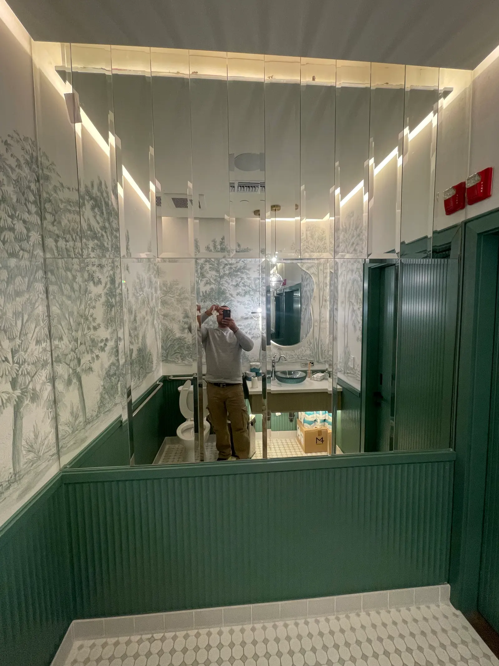 Clear glass partition panels above green panelled wainscot in a wallpapered powder room