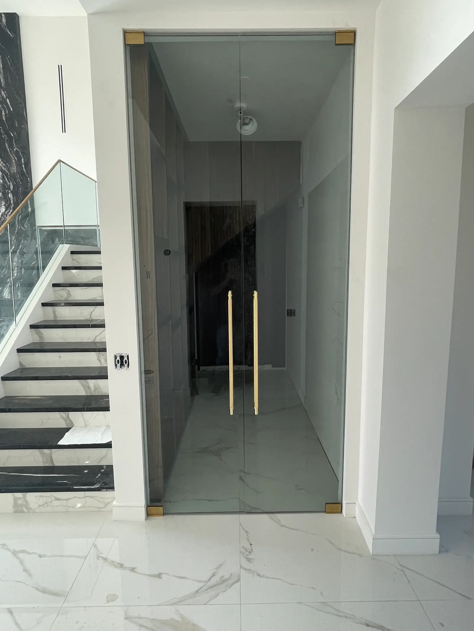 Double frameless glass doors with full-height brass pulls opening off a marble entry