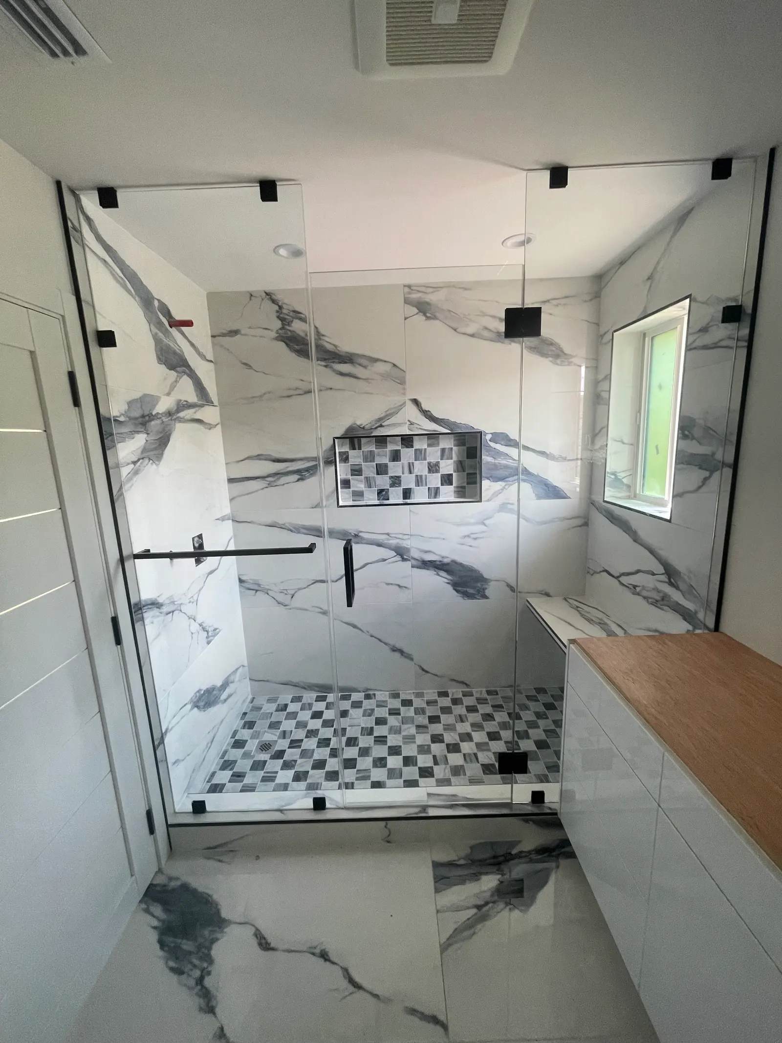 Frameless shower enclosure with matte-black hardware, a marble bench and a checkerboard mosaic pan