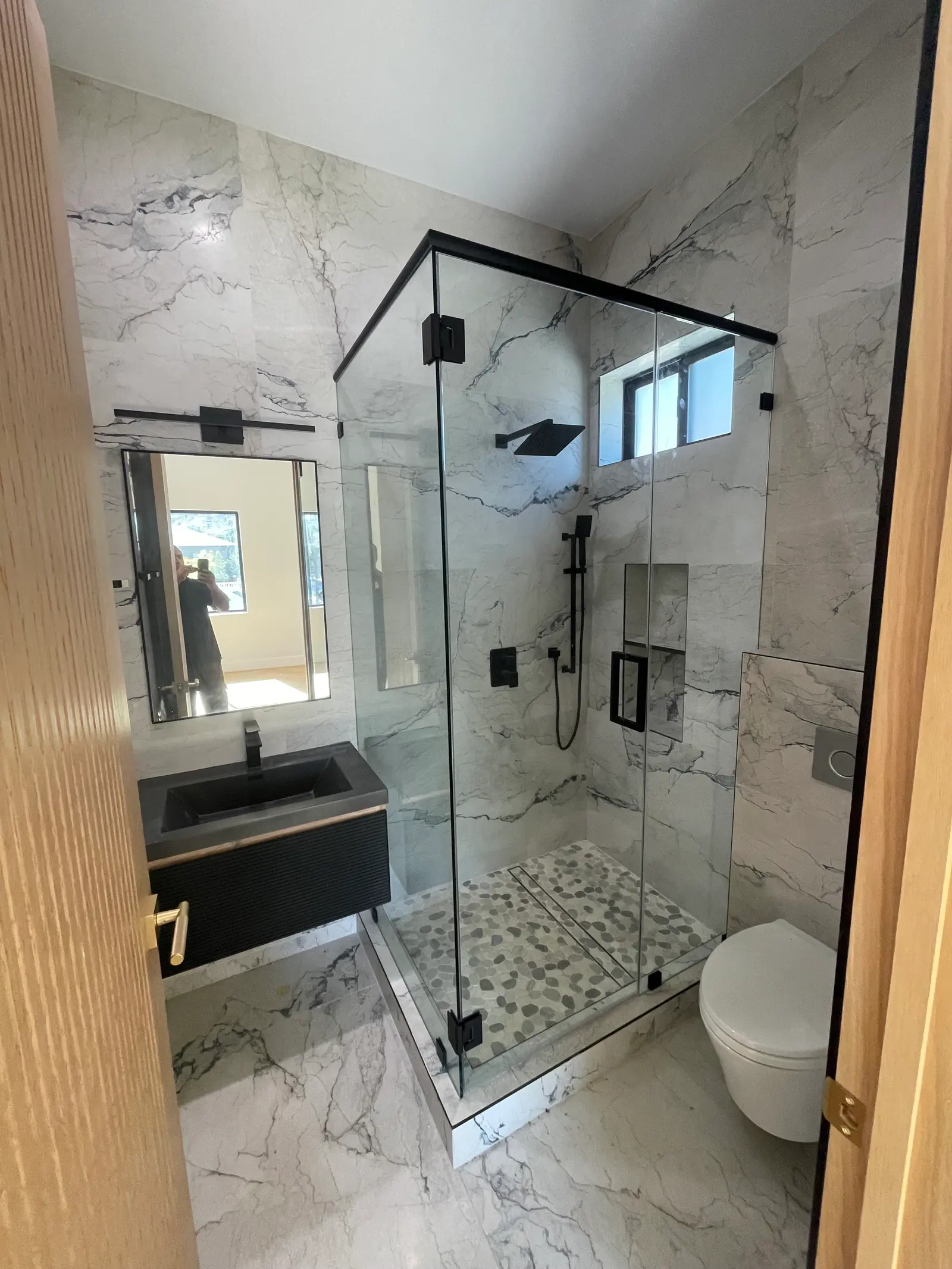 Neo-angle frameless shower with matte-black hardware, marble walls and a black floating vanity