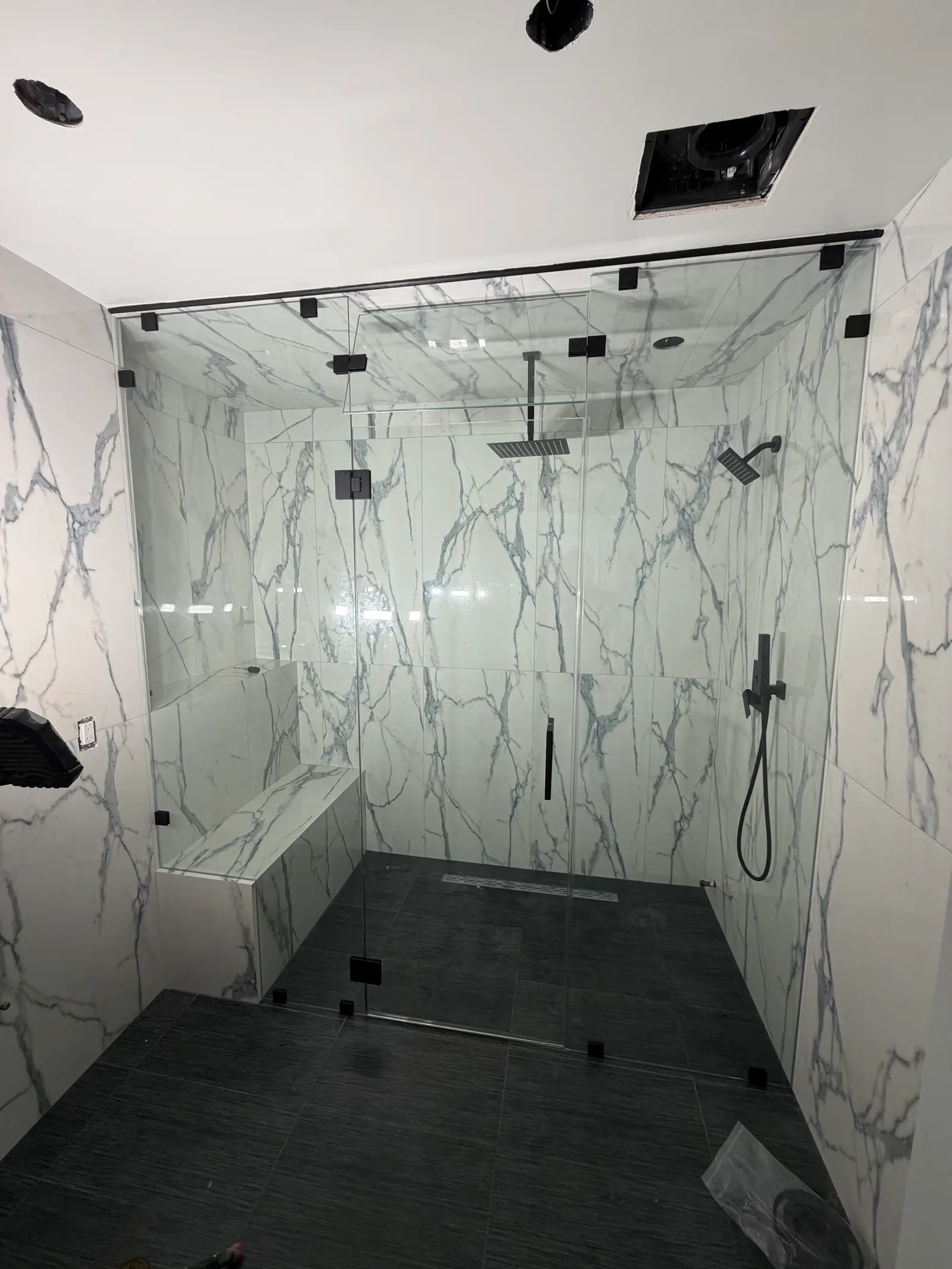 Frameless steam-shower enclosure with matte-black hardware, a marble bench and a slate floor