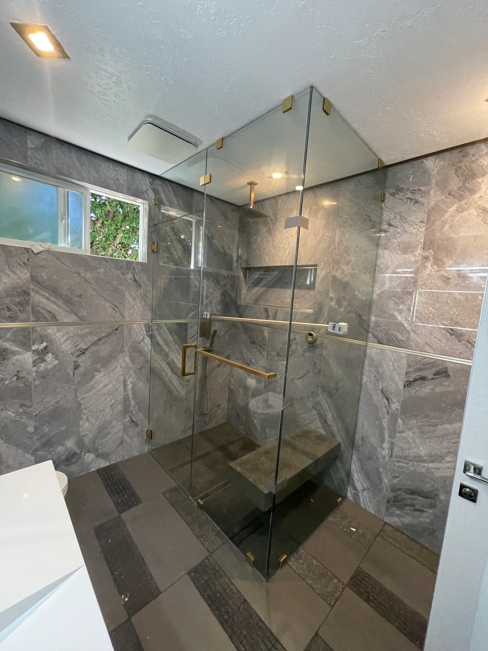 Frameless corner shower with brushed-brass hardware, a built-in stone bench and gray marble walls