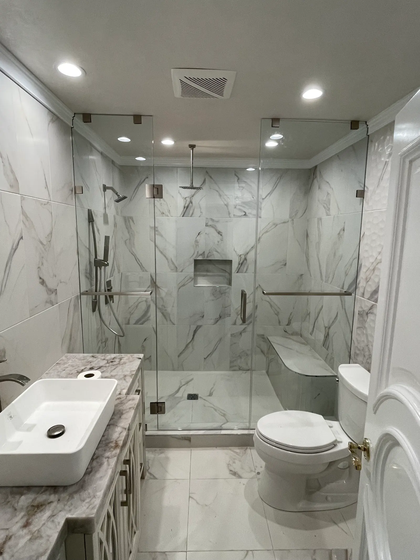 Frameless shower door and return panel with chrome hardware in a white marble bathroom