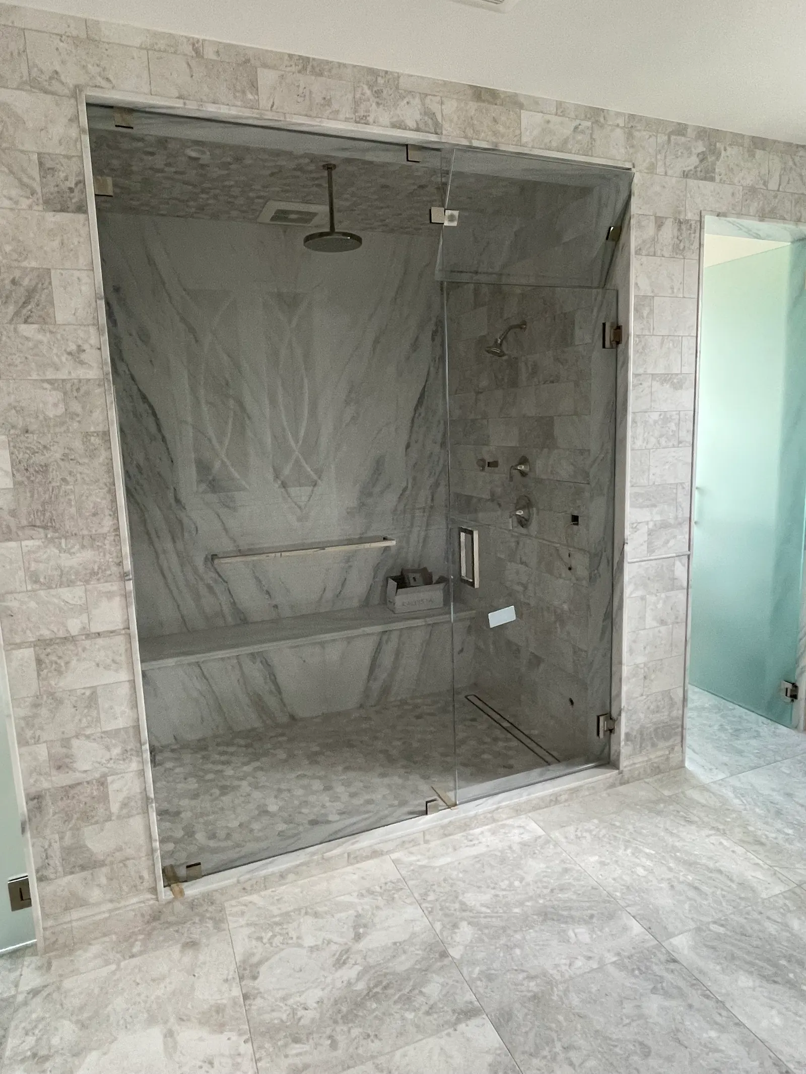 Full-height frameless steam-shower enclosure with a marble bench and transom panel