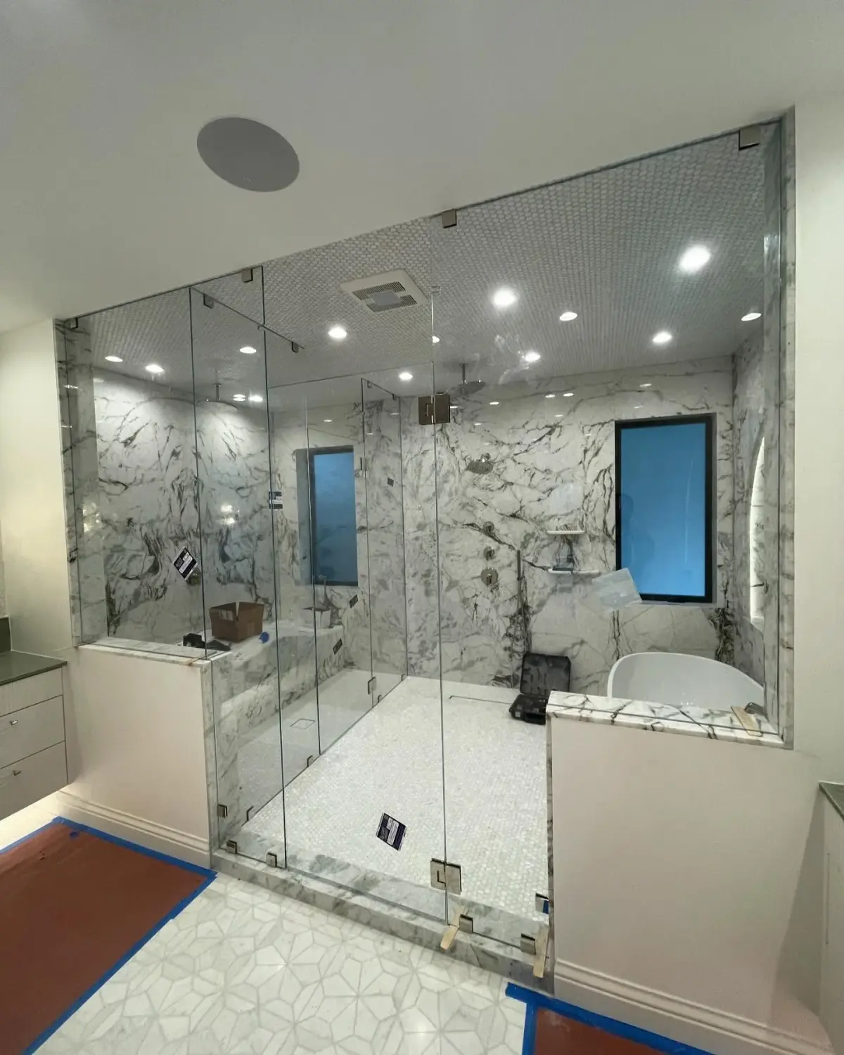 Floor-to-ceiling glass steam-shower enclosure with polished-nickel hinges in a marble primary bathroom