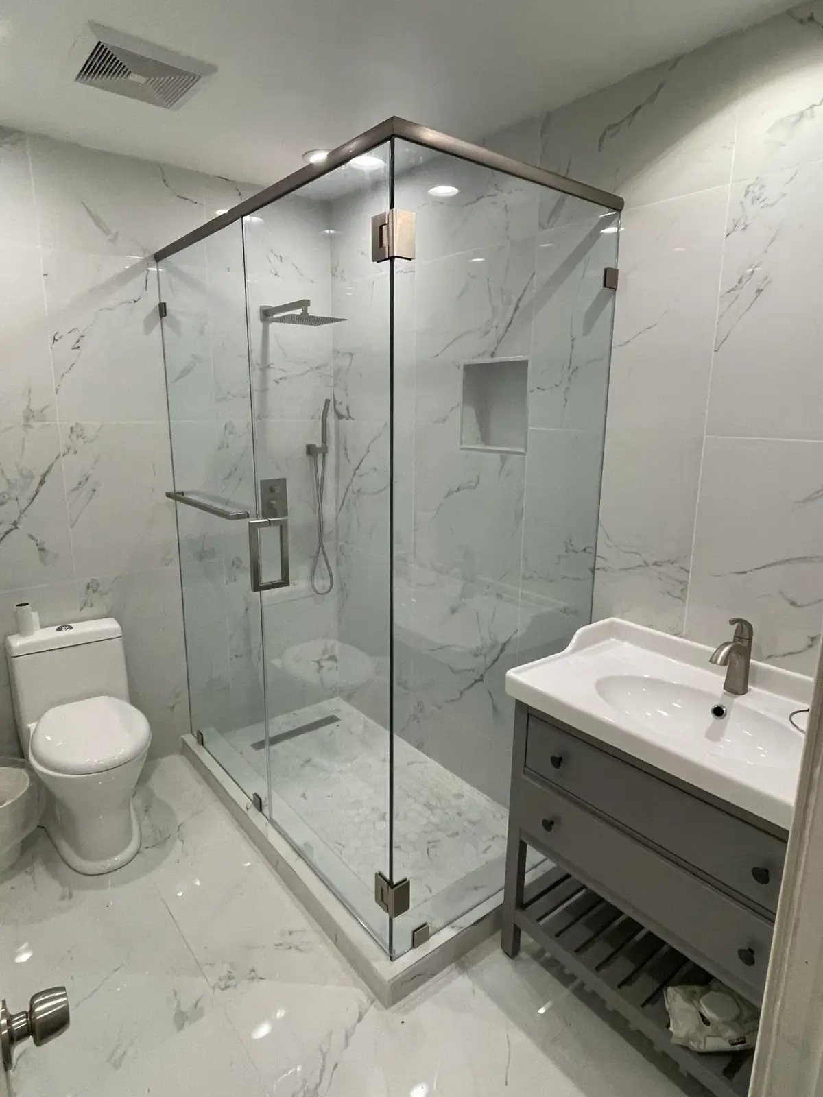 Frameless corner shower with a brushed-nickel header and hinges in a white marble bathroom